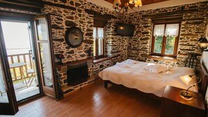 A cozy room with stone walls, a fireplace, a bed, and a television. - Eudora - Mansion (Zagora-Mouresi)