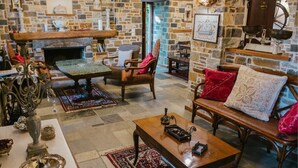 A cozy room with a stone wall, a fireplace, a wooden table, and a bench with red cushions. - Eudora - Mansion (Zagora-Mouresi)