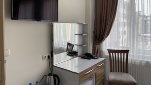 Une chambre d’hôtel équipée d’une télévision à écran plat, d’une coiffeuse avec un miroir, d’un bureau avec un téléphone et d’une chaise.