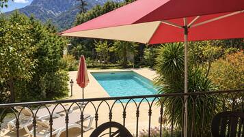 Un espace piscine avec une vue imprenable sur les montagnes, entouré d’une végétation luxuriante et agrémenté de chaises longues et d’un parasol rouge.