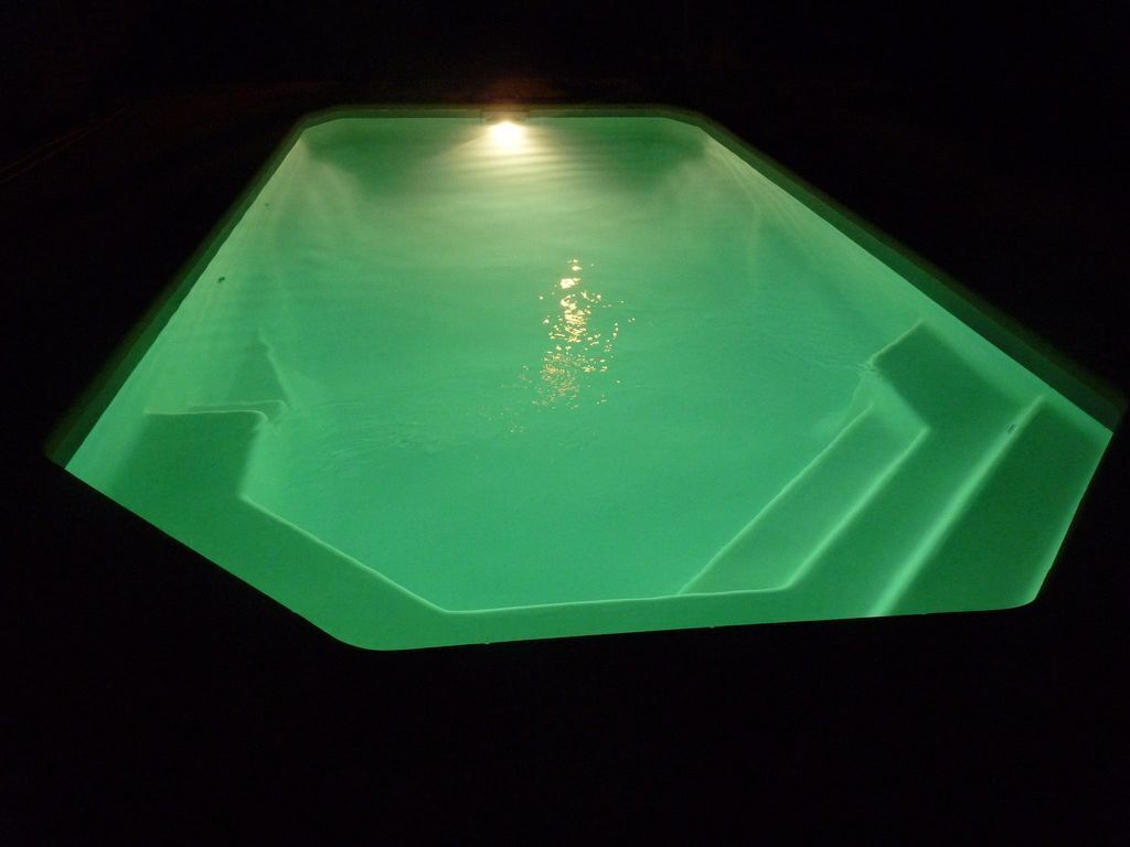 En grön, rektangulär pool med en central ljuskälla som reflekteras på vattenytan.
