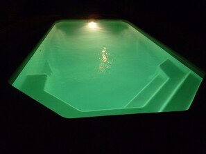 Une piscine rectangulaire de couleur verte, avec une source de lumière centrale dont les rayons se reflètent à la surface de l’eau.