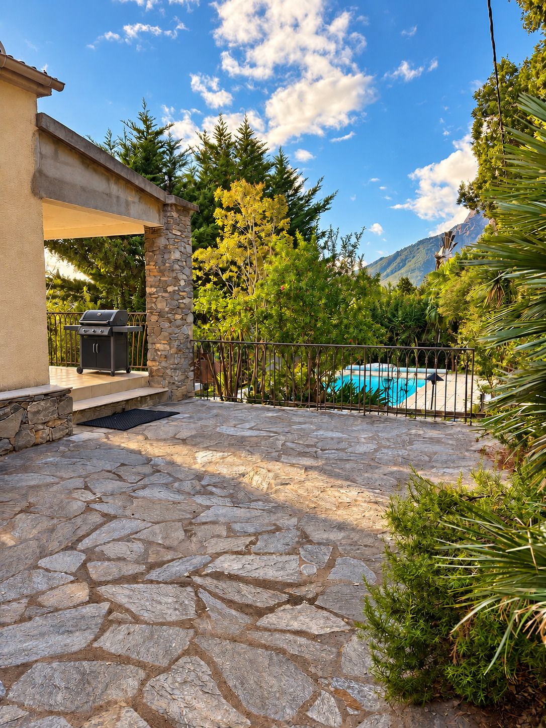 Une terrasse en pierre avec un barbecue, une piscine et un mur en pierre.