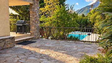 Une terrasse en pierre avec un barbecue, une piscine et un mur en pierre.