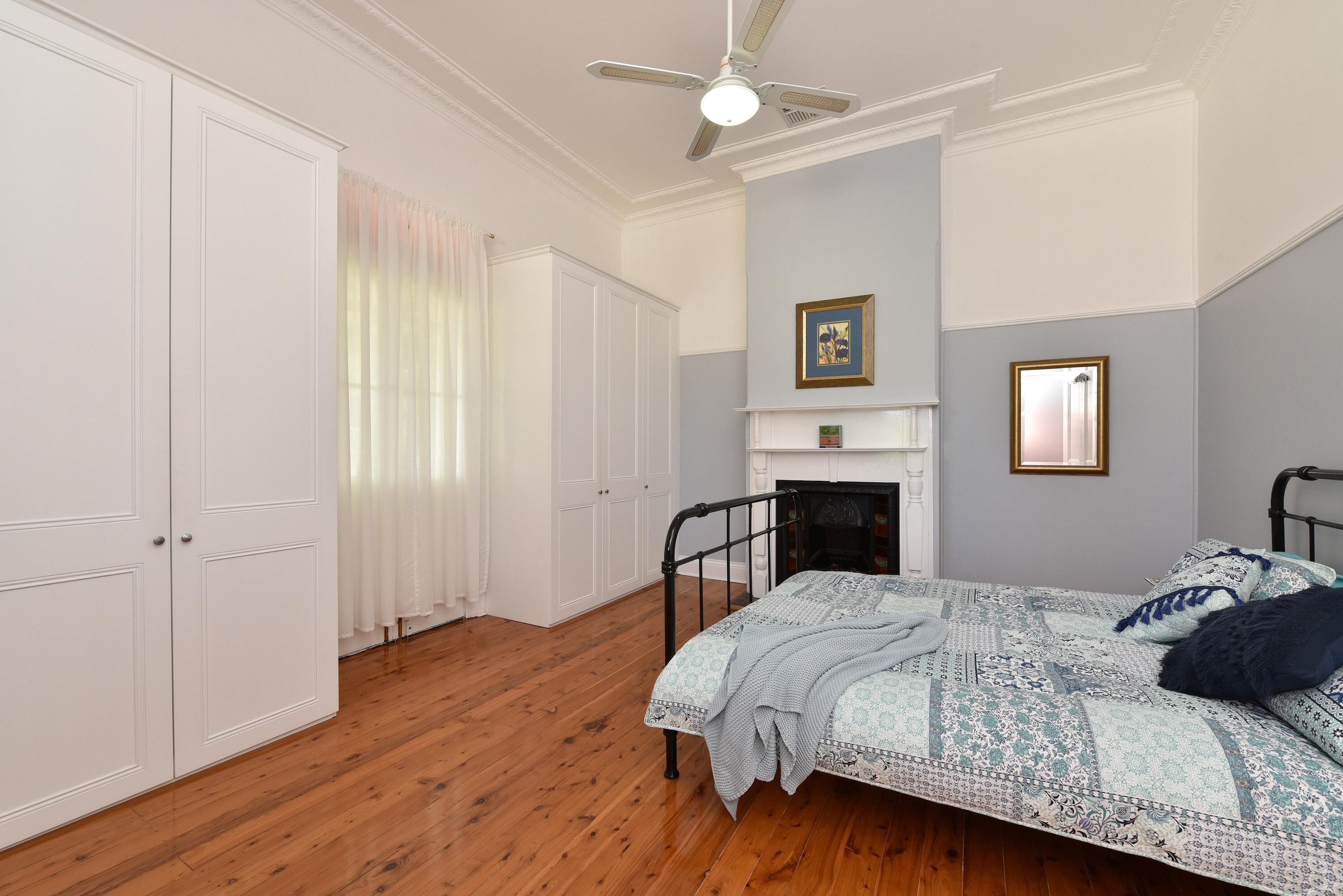 A bedroom with a bed, a fireplace, a ceiling fan, and a wardrobe.