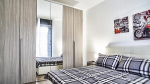 A modern bedroom with a large mirror, a bed with plaid bedding, and a wall-mounted motorcycle poster. - B&B La Casa dei Miraglia San Cataldo (San Cataldo)