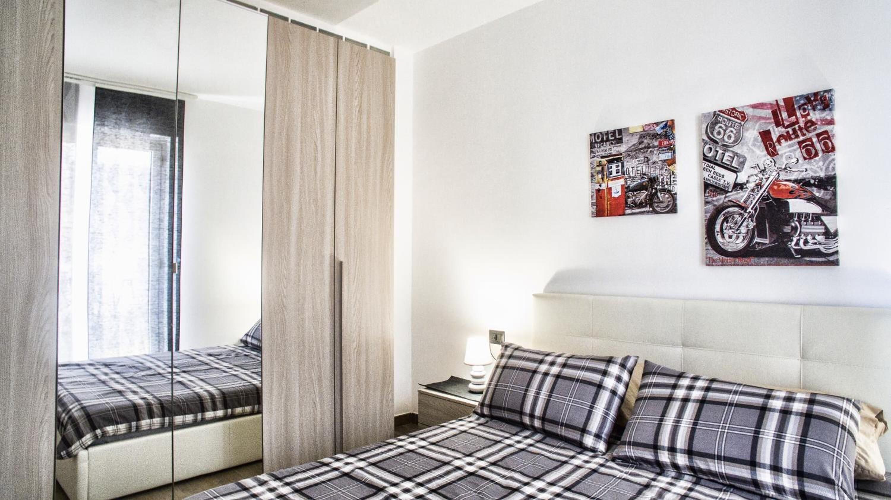 A hotel room with a bed, a nightstand, a lamp, and two wall art pieces depicting motorcycles.