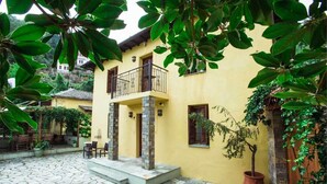 A yellow building with a balcony, stone flooring, and potted plants. - Guesthouse Ellis (Zagora-Mouresi)
