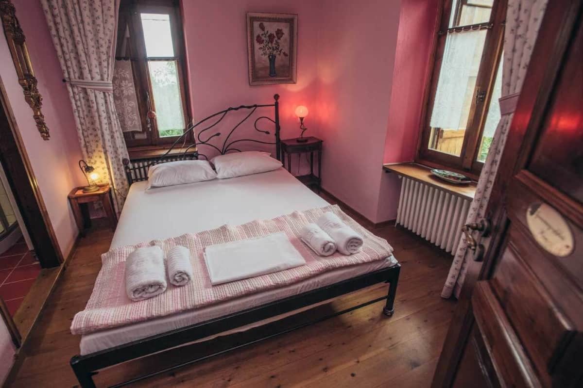 Ein Schlafzimmer mit einem Bett, einem Nachttisch mit Lampe, einem Heizkörper und einem Fenster mit Vorhängen.