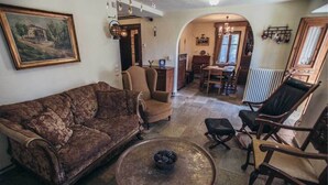 A cozy living room with a vintage sofa, a coffee table, and wooden chairs. A dining area with a table and chairs is visible in the background. - Guesthouse Ellis (Zagora-Mouresi)