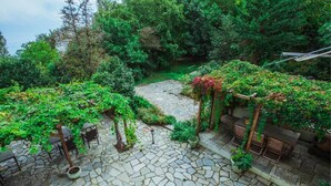 A stone-paved courtyard with a stone pathway, wooden furniture, and lush greenery. - Guesthouse Ellis (Zagora-Mouresi)