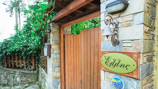 A stone building with a wooden door, a green sign reading "Eddns," and a bell on the wall. - Guesthouse Ellis (Zagora-Mouresi)