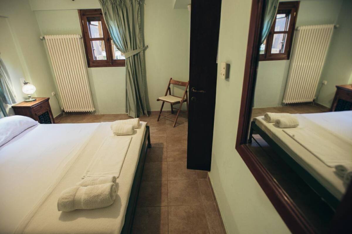 Ein Hotelzimmer mit zwei Betten, einem Sessel, einem Nachttisch aus Holz mit Lampe und einem Fenster mit Vorhängen.