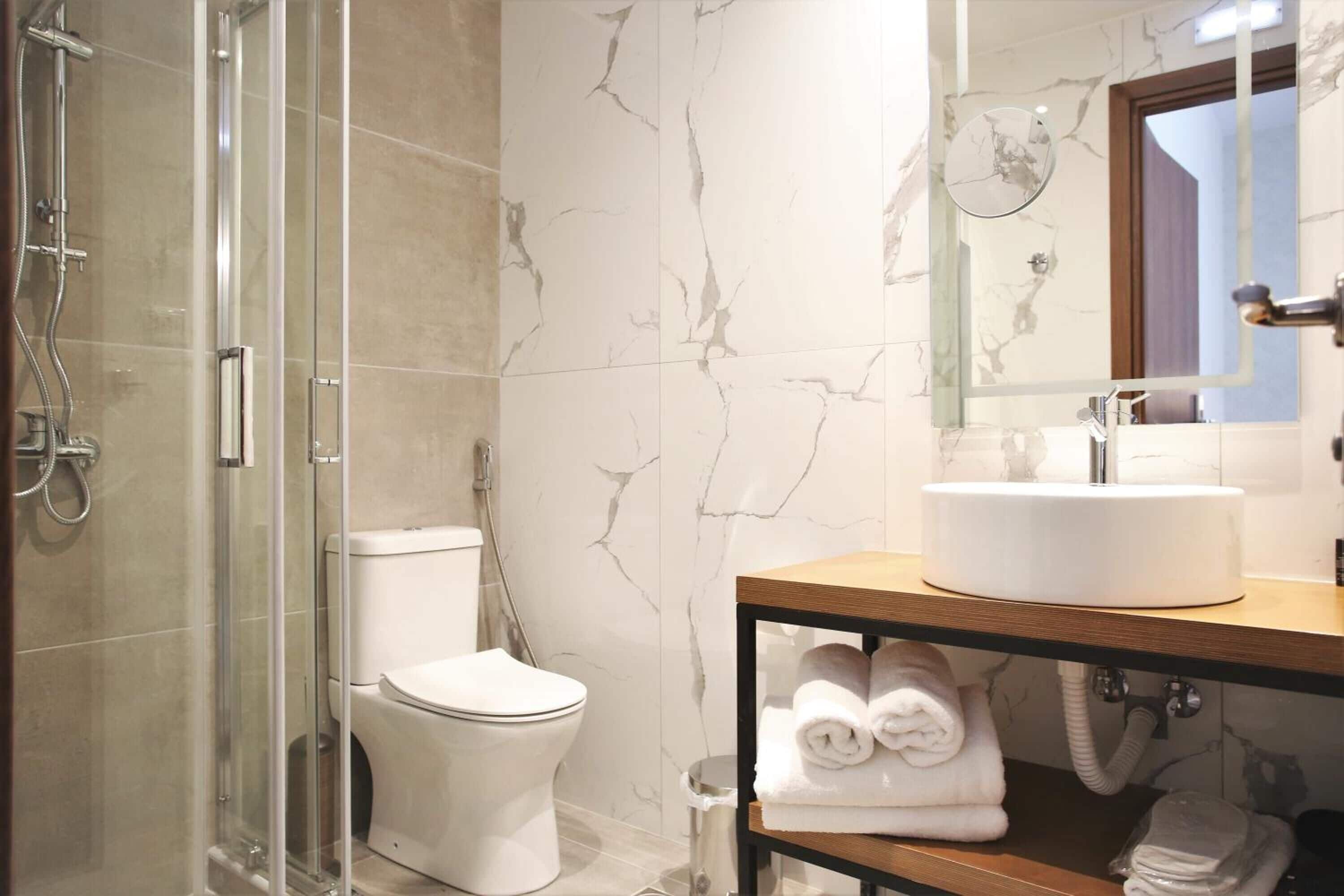 Un baño con ducha envuelta en vidrio, inodoro blanco y salpicadero de mármol.