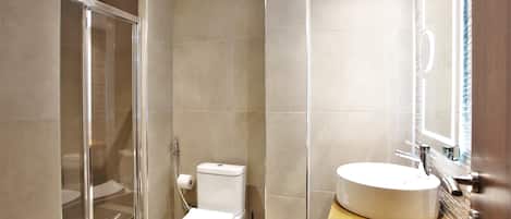 A bathroom with a glass-enclosed shower, a toilet, and a sink with a mirror above it.
