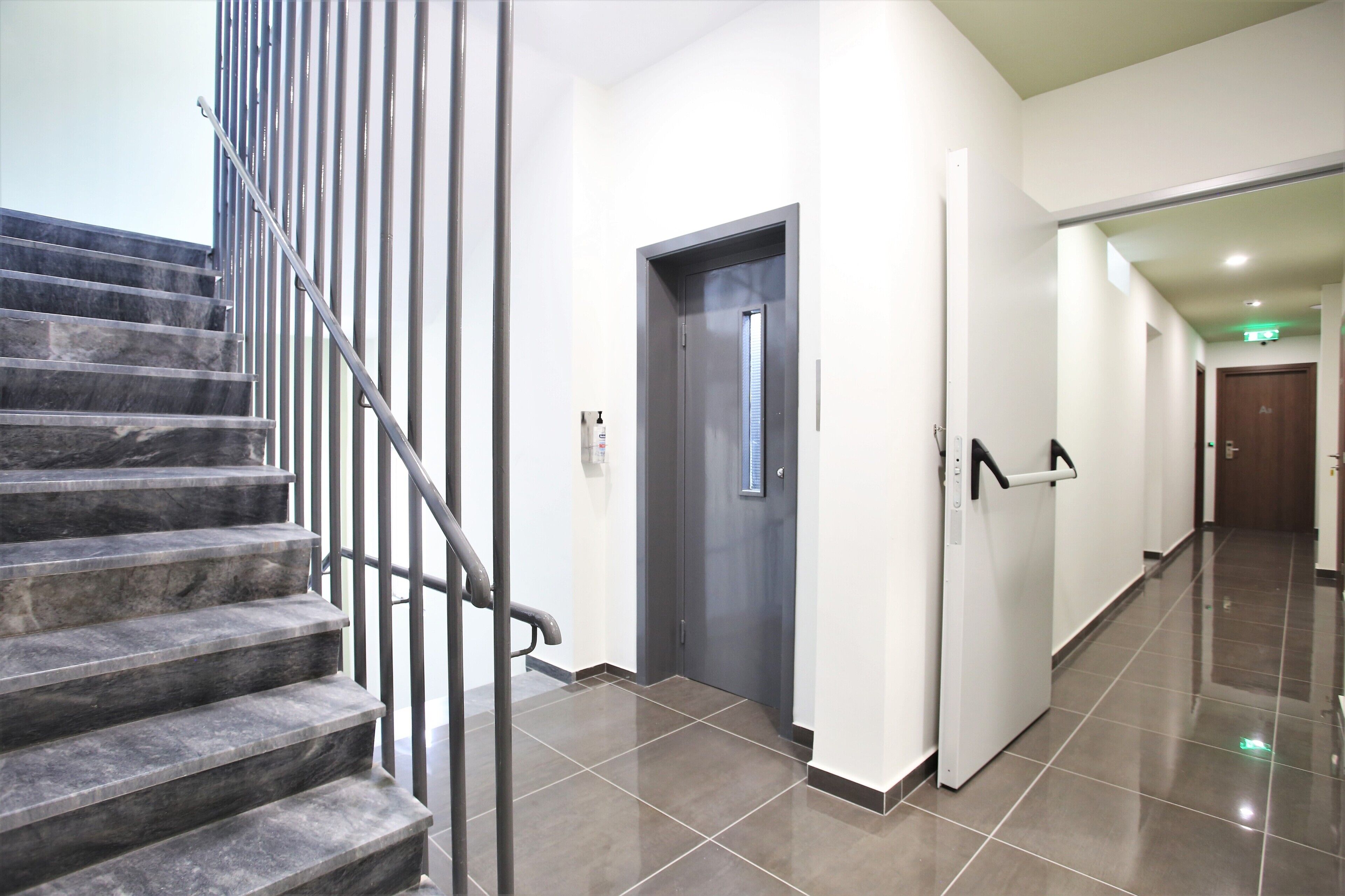 Un couloir propre et moderne, avec un escalier en marbre, une porte dotée d’une poignée et une main courante.