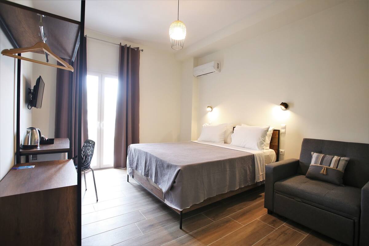 Une chambre à coucher comprenant un lit, une table de chevet, une chaise et un bureau avec un porte-manteau suspendu.