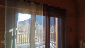 A room with large windows, a wooden deck, and a view of a mountainous landscape.