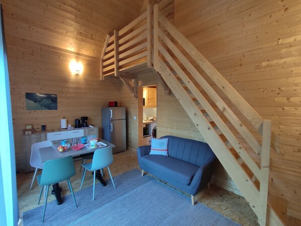 Un interior de cabaña acogedor con comedor, sofá, escalera y cocina.