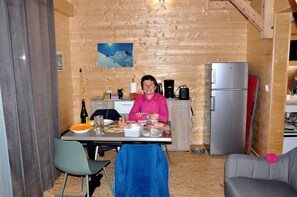 Een houten interieur met een eettafel gedekt voor twee personen, een koelkast en een keukenhoek.