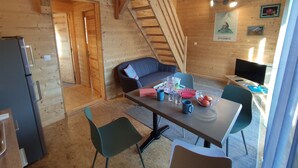A cozy cabin interior with a dining table, chairs, a sofa, a TV, and a staircase.