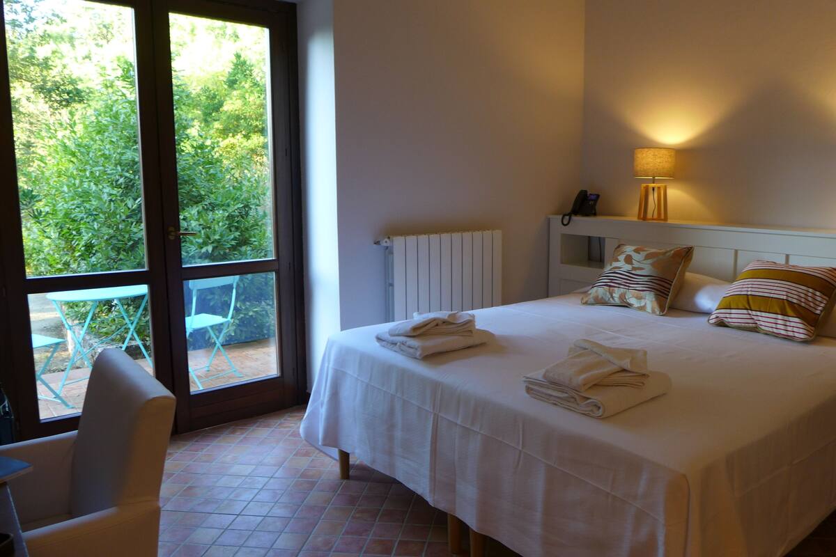 Un lit bien fait, agrémenté de serviettes, une lampe de chevet et une vue sur la verdure à l’extérieur.