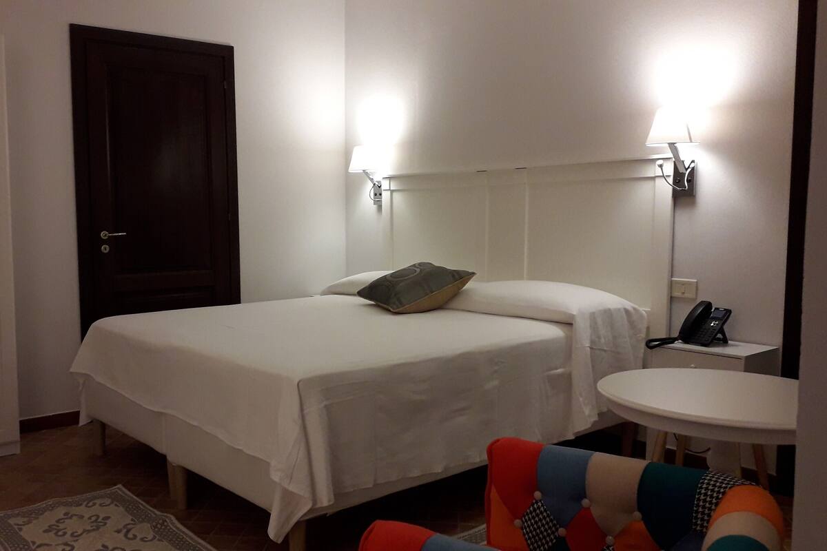 Une chambre d’hôtel comprenant un lit, une table de chevet, une lampe, un téléphone et une chaise.