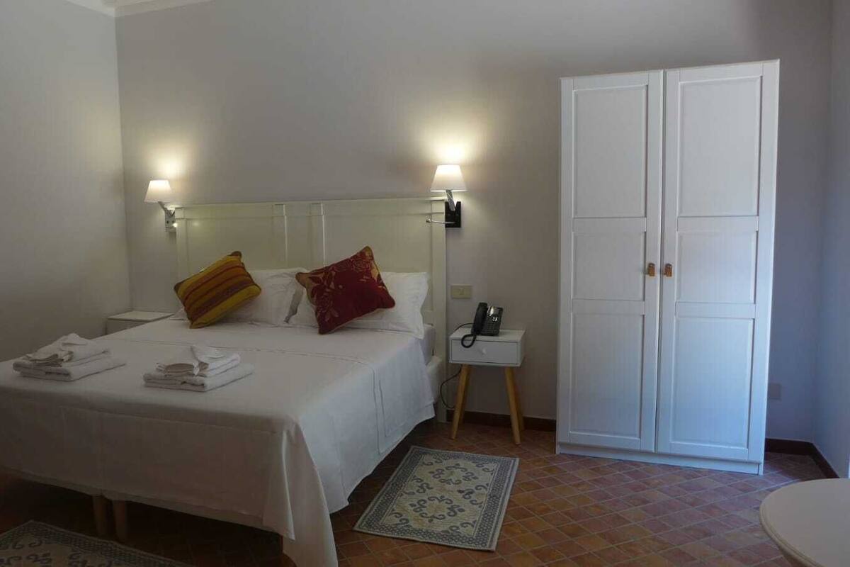 Une chambre d’hôtel comprenant un lit, une table de chevet, une lampe, une armoire et un petit tapis.