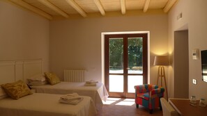 A hotel room with two beds, a chair, a table, a lamp, and a view of the outdoors through a glass door. - Chiosi Country Club (Corleone)