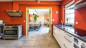 Una cucina moderna con piano cottura a gas, forno e cappa aspirante in acciaio inox. È presente una zona pranzo con tavolo e sedie, e si intravede un'altra stanza attraverso un'apertura.