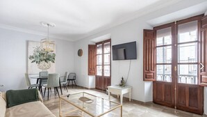 A living room with a sofa, a glass coffee table, a dining table with chairs, a TV mounted on the wall, and large wooden doors. - Mirador San Jeronimo-Cathedral CTH Granada (Granada)