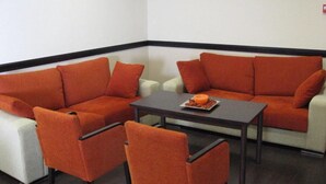 A corner seating area with orange sofas and chairs, a small table, and a white couch. - Hotel Machaco (Alburquerque)