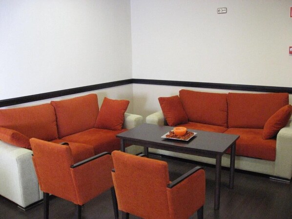 A corner seating area with orange sofas and chairs, a small table, and a white couch.