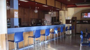 A bar area with a counter, blue chairs, and a television screen. - Hotel Machaco (Alburquerque)