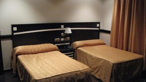 A hotel room with two single beds, a nightstand with a lamp, and a curtain on the window. - Hotel Machaco (Alburquerque)