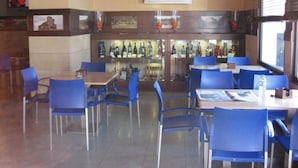 A restaurant with blue chairs and tables, a bar area with bottles, and a television on the wall. - Hotel Machaco (Alburquerque)