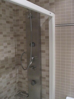 A shower enclosure with a glass door, a handheld showerhead, and a wall-mounted faucet.