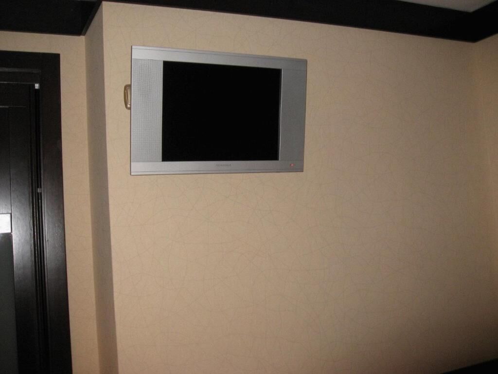 Un televisor de pantalla plana montado en la pared en una habitación con paredes color beige y una puerta oscura.