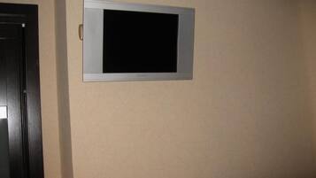 Un televisor de pantalla plana montado en la pared en una habitación con paredes color beige y una puerta oscura.