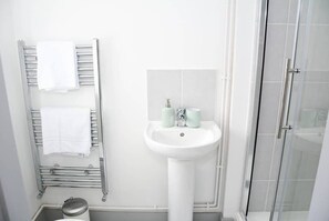 A bathroom with a white sink, a towel rack with two towels, and a glass shower enclosure. - Pearl House Cardiff -  Apartment 3 (Cardiff)
