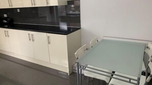 A kitchen with white cabinets and a black countertop, a glass table with four chairs, and a white radiator. - Wellfield Blooms Cardiff Romantic Room (Cardiff)