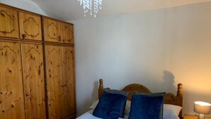 A bedroom with a wooden wardrobe, a bed with blue bedding, and a bedside lamp. - Wellfield Blooms Cardiff Romantic Room (Cardiff)