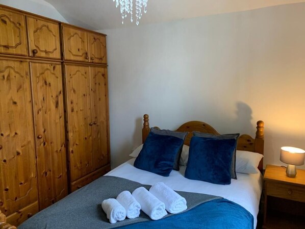 A bedroom with a wooden wardrobe, a bed with blue bedding, and a bedside lamp.