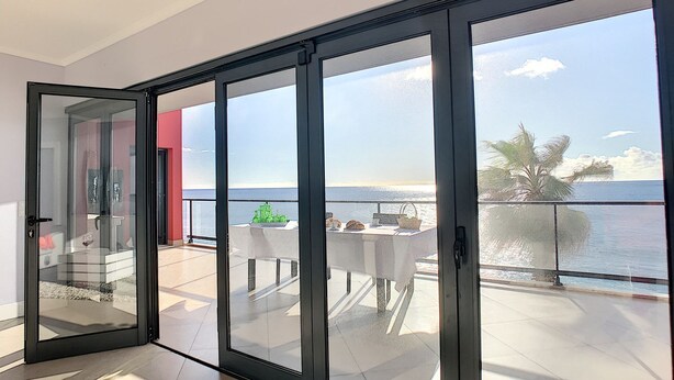 Un balcon spacieux avec vue sur la mer, une table à manger et une porte vitrée donnant sur l’intérieur.