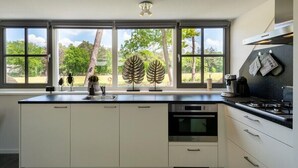 Une cuisine moderne dotée d’une grande fenêtre, de meubles blancs et d’une cuisinière à gaz.