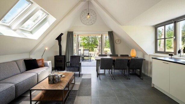 Un loft moderne doté d’un plafond haut, de fenêtres de toit, d’une cheminée, d’un coin repas et d’une cuisine.