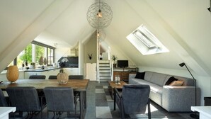 Un espace de vie aménagé sous les combles, comprenant un coin repas, un canapé et un escalier.
