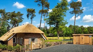 Une petite maison rustique, dotée d’un toit de chaume, entourée d’une clôture en bois et bordée d’une allée en gravier.
