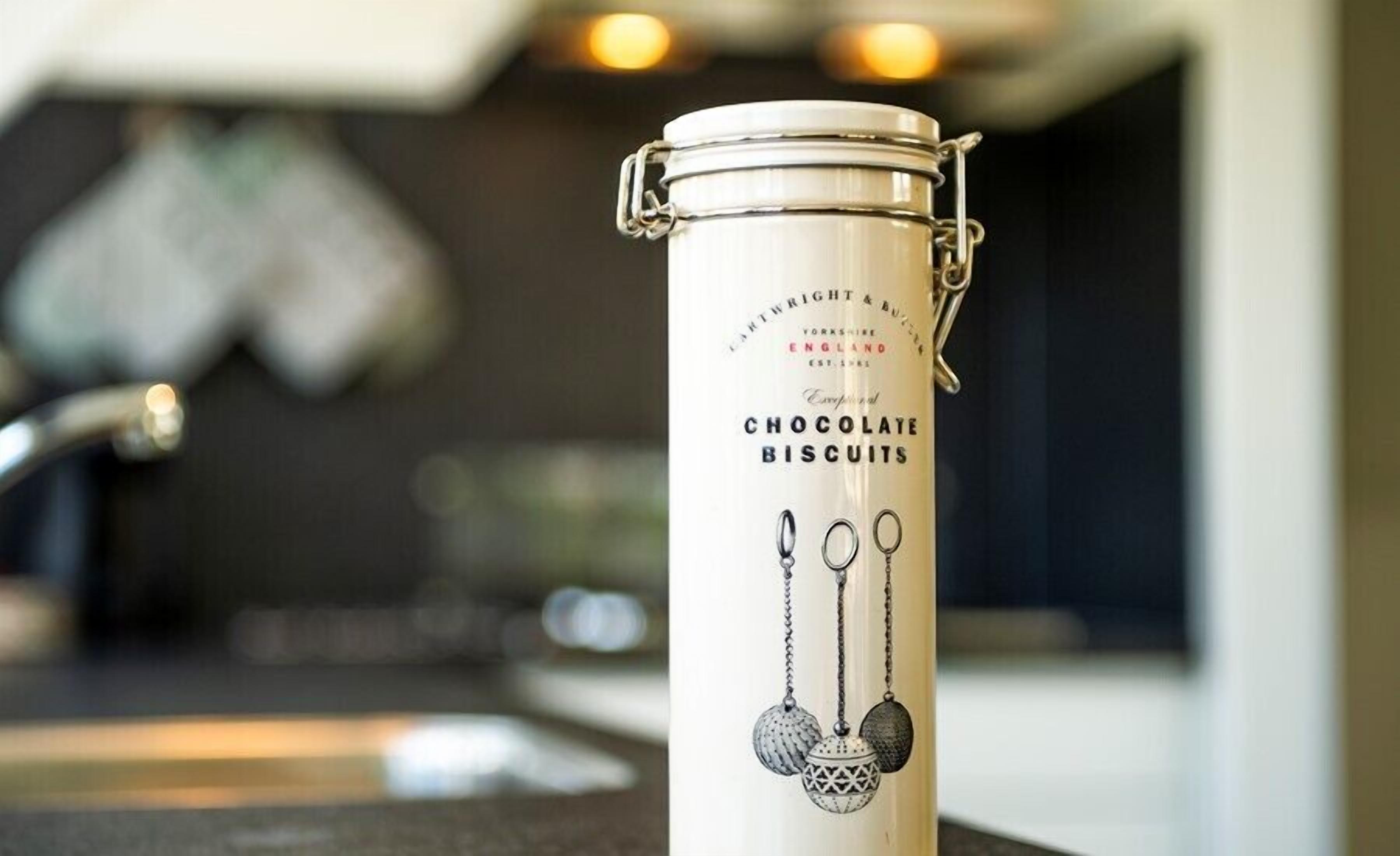 A stainless steel container with a lid, labeled 'CHOCOLATE BISCUITS,' placed on a kitchen counter.