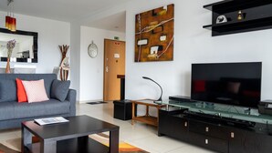 A modern living room with a grey sofa, a coffee table, a flat-screen TV, a glass-top coffee table, and a black entertainment unit.